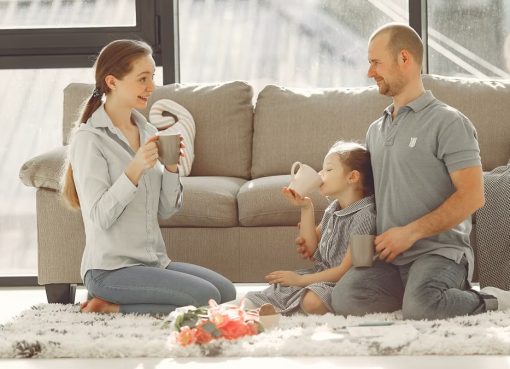 Cheerful family drinking tea in living room while having rest and laughing together during weekend while spending time and having fun